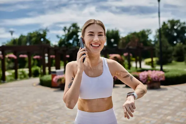 Uma jovem em activewear, com vitiligo, fala ao telefone enquanto sorri em um parque. — Fotografia de Stock