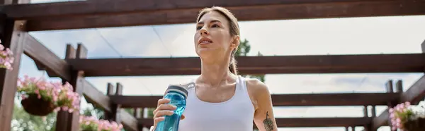 A young woman with vitiligo drinks water after a vigorous outdoor workout under a park pergola. — Stock Photo
