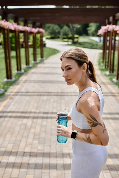 A young woman with vitiligo takes a break from her workout, holding a water bottle and looking ahead. — Stock Photo