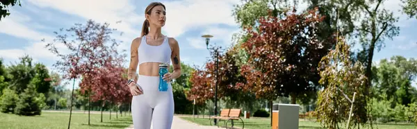 Una giovane donna con vitiligine cammina in un parco mentre tiene in mano una bottiglia d'acqua, esercitandosi all'aperto nel pomeriggio. — Foto stock