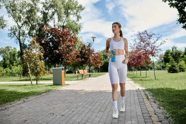 A young woman with vitiligo walks in a park, holding a water bottle in her hand. — Stock Photo