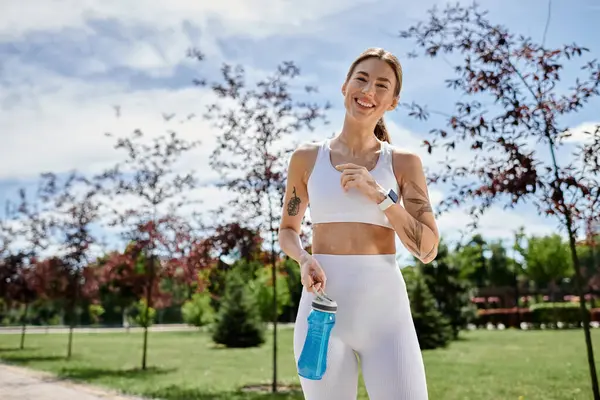 A young woman with vitiligo smiles as she walks through a park during her workout. — Stock Photo