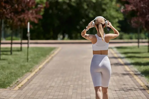 A young sportswoman with vitiligo walks through a park on a sunny day, wearing headphones and activewear. — Stock Photo