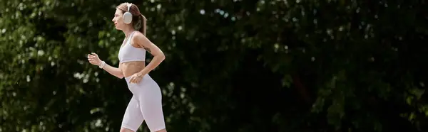 A young woman with vitiligo runs through a park, wearing active wear and headphones. — Stock Photo