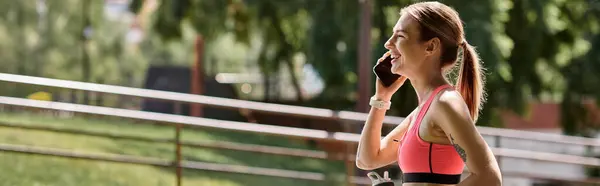 Una giovane donna in reggiseno sportivo rosa parla al telefono mentre si prende una pausa dal lavoro in un parco. — Stock Photo