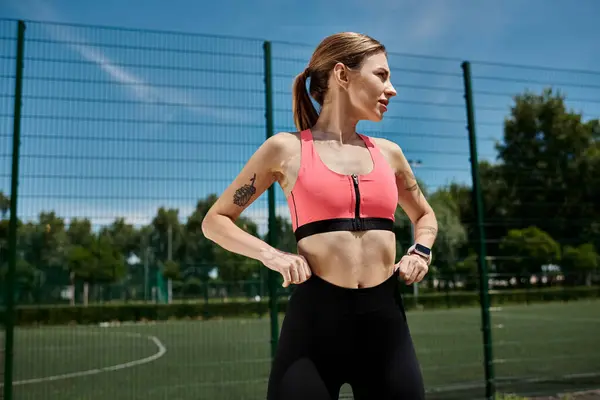 A young woman in pink activewear stands on a soccer field, hands on her hips, looking determined. — Stock Photo