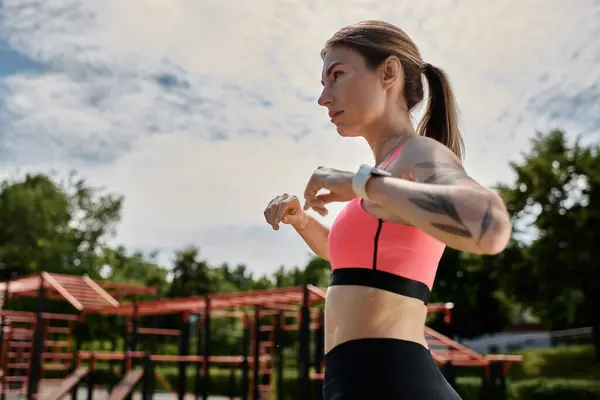 Una joven con vitiligo en un sujetador deportivo rosa comprueba su reloj antes de hacer ejercicio en un gimnasio al aire libre. — Stock Photo