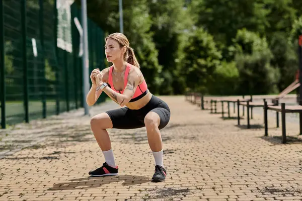 A young woman with vitiligo performs squats in a park while wearing a pink crop top and black shorts. — Stock Photo
