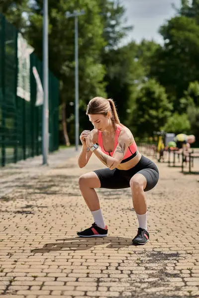 A young woman with vitiligo in a pink crop top performs squats in a park, sunlight illuminating her workout. — Stock Photo