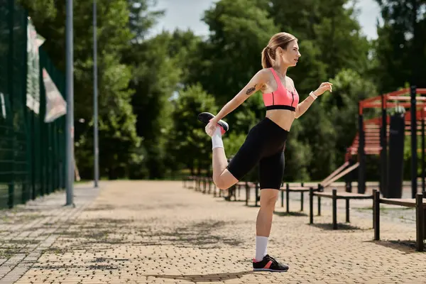A young woman with vitiligo stretches her leg while wearing a pink crop top and black shorts in a park. — Stock Photo