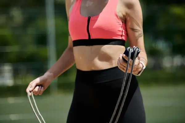 A young woman with vitiligo wears a pink crop top and black leggings as she prepares to jump rope outdoors in a park. — Stock Photo