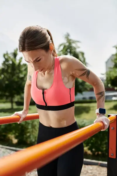 A young woman in pink top and black leggings does dips on a bar in a park, showing strength and determination — Stock Photo