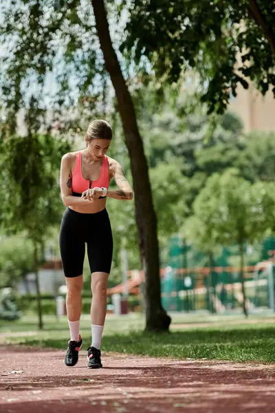 A young woman with vitiligo, wearing a pink crop top and black shorts, checks her wristwatch after exercising in a park. — Stock Photo