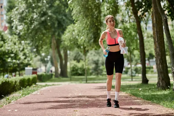 A young woman with vitiligo walks along a park path, holding a water bottle and a towel. — Stock Photo