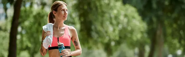 Una giovane donna con la vitiligine, indossando un crop top rosa e abbigliamento attivo, prende una pausa dal suo allenamento in un parco. — Foto stock