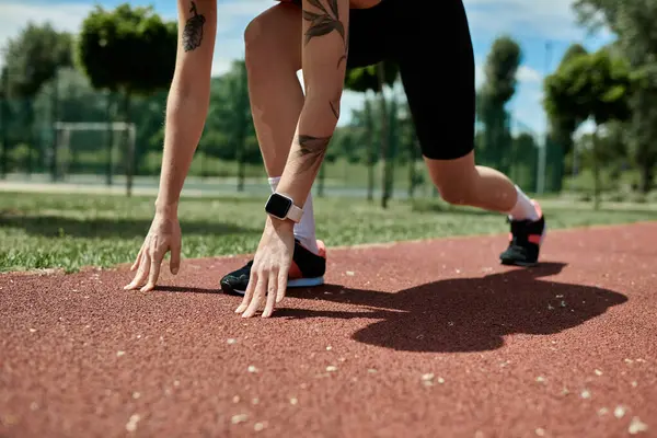 Una giovane donna con la vitiligine e un tatuaggio in abbigliamento attivo si prepara a correre su una pista, con la mano protesa verso terra. — Foto stock