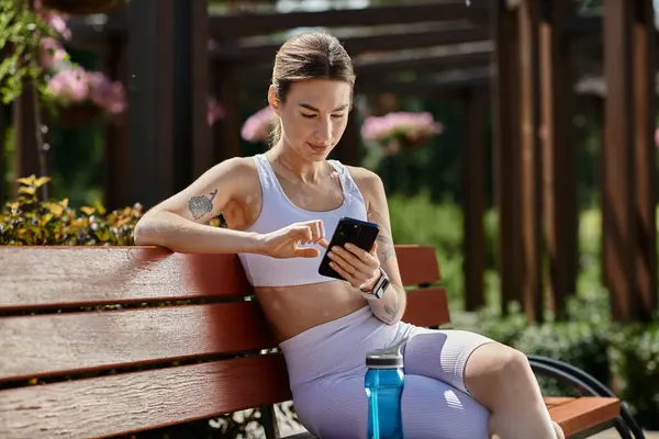 Jeune femme avec vitiligo assis sur un banc de parc, vérifier son téléphone après une séance d'entraînement. — Photo de stock