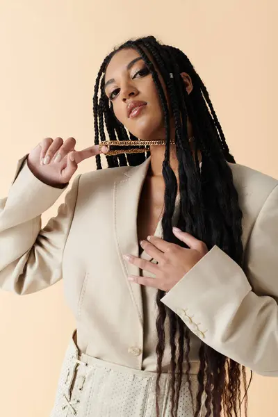 A young woman with long braids poses in a cream blazer and matching pants, her confident gaze meeting the camera. — Stock Photo