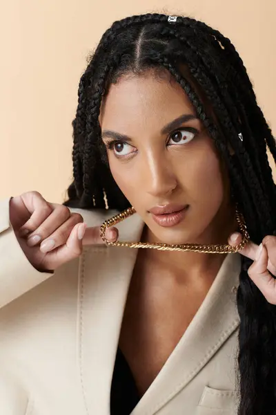 A young African American woman with long braids poses in a beige blazer, wearing a gold chain. — Stock Photo