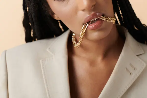 A young woman with braided hair bites down on a gold chain. — Stock Photo