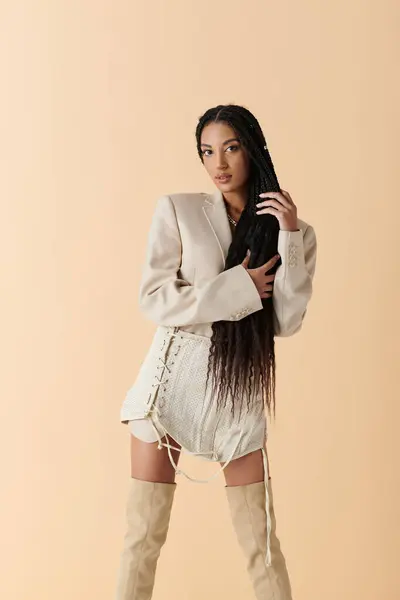 Confident African American woman in her 20s, stylishly posing with long black hair, wearing cream blazer, shorts, and knee-high boots — Stock Photo