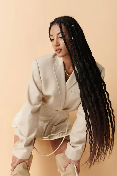 A young woman with long black braids poses in a beige blazer, skirt, and thigh-high boots. — Stock Photo