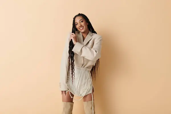 A young woman with long black braids poses confidently in a fashionable outfit against a beige backdrop. — Stock Photo