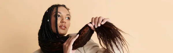 A young woman with braided hair poses confidently against a beige backdrop, showcasing her vibrant and stylish personality. — Stock Photo