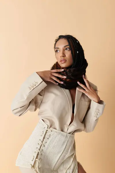 A young African American woman wearing a cream blazer and lace-up skirt poses against a beige backdrop. — Stock Photo