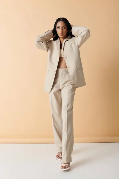 A young woman in a beige suit stands confidently against a pale background. — Stock Photo