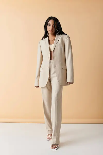 A young woman poses confidently in a beige suit against a neutral background. — Stock Photo