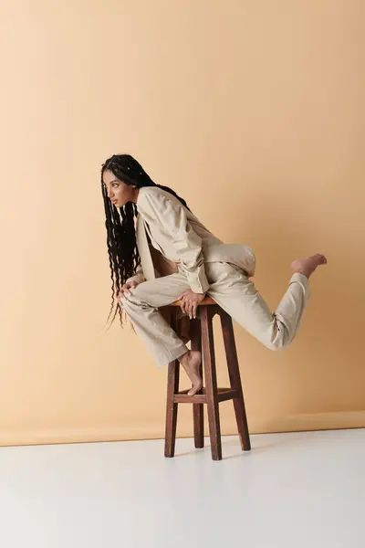 Une jeune femme dans une tenue élégante s'assoit sur un tabouret en bois avec sa jambe étendue, regardant de côté. — Photo de stock