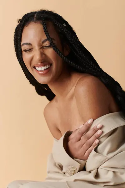 A stylish young Black woman with braids smiles warmly in a beige outfit against a soft, neutral backdrop, showcasing her radiant beauty — Stock Photo