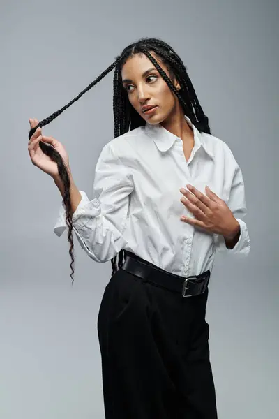 A young African American woman in a white shirt poses against a grey backdrop, her braids cascading down her back. — Stock Photo
