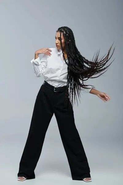 A young African American woman with long braids poses in a white shirt and black pants. — Stock Photo