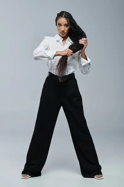 Femme afro-américaine confiante pose avec des cheveux et chemise blanche devant fond gris — Photo de stock