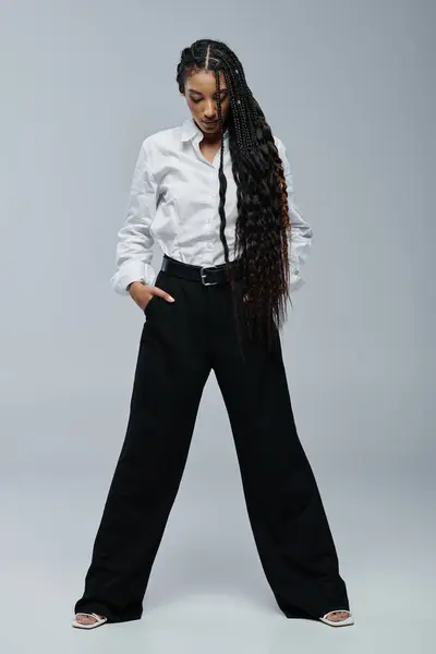 A young woman with long braids poses in a white shirt and black pants. — Stock Photo