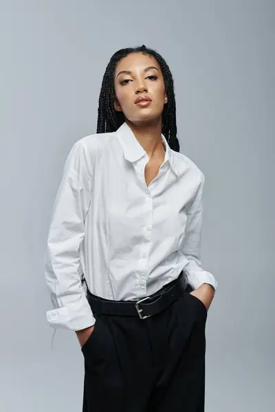 A young African American woman poses in a stylish white shirt against a grey background. — Stock Photo