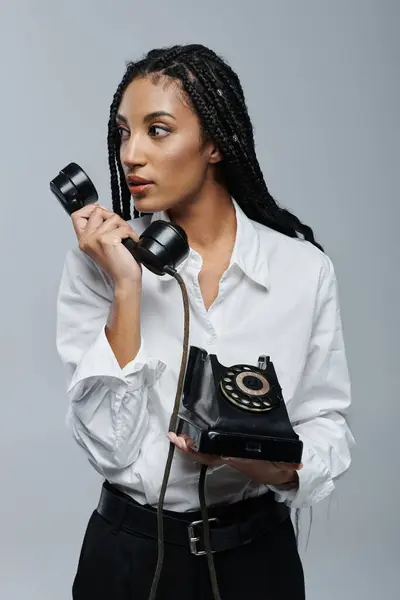 A stylish woman with braids speaks on a rotary phone, her expression both curious and intrigued. — Stock Photo