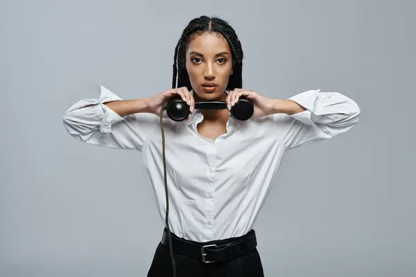 A young woman with braids holds a black rotary phone to her neck, her serious expression suggests she is ready for a call. — Stock Photo