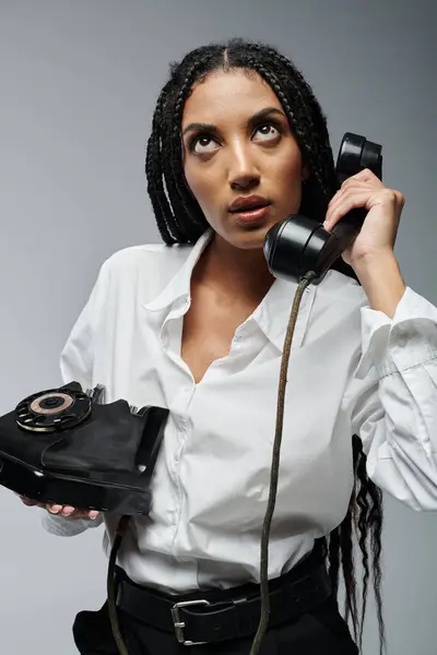 A young Black woman with long braids, wearing a white button-down shirt and black pants, speaks on an old-fashioned rotary phone. — Stock Photo
