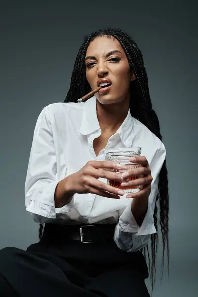 A stylish African American woman in a white shirt and black pants poses with a glass of liquor — Stock Photo