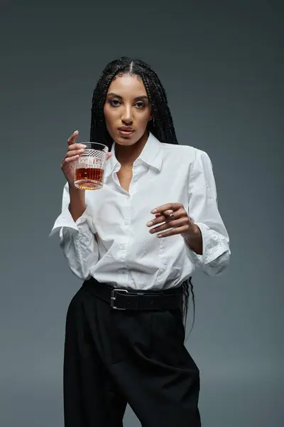 Une femme élégante dans une chemise blanche tient un verre de whisky tout en regardant la caméra. — Photo de stock