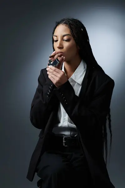 A young woman in a black blazer and white shirt lights a cigarette with a silver lighter. — Stock Photo