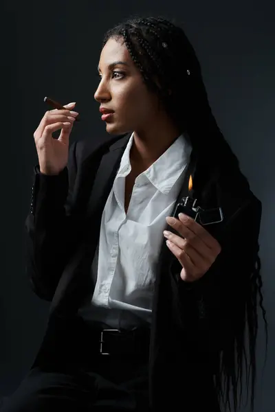 A young woman in a white shirt and black blazer poses against a gray background, holding a lighter and a cigarette. — Stock Photo