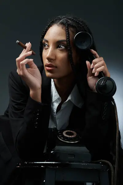 Uma mulher elegante em uma camisa branca e blazer preto se inclina de volta em uma cadeira, segurando atenciosamente um telefone e charuto. — Fotografia de Stock