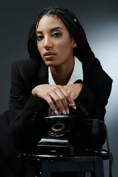 A young woman with braids, wearing a white shirt and black blazer, poses with her hands on a vintage rotary phone. — Stock Photo
