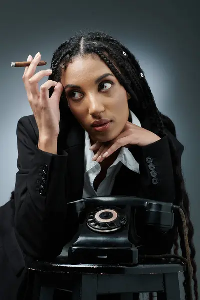A woman with braids, wearing a white shirt and black blazer, poses with her hands on a vintage phone with cigar in hand — Stock Photo