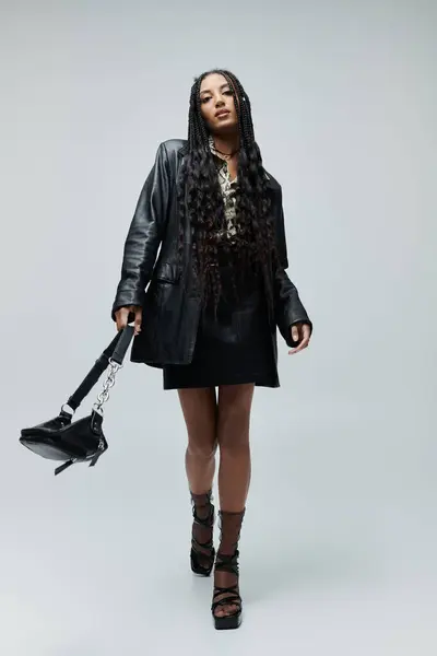A young Black woman in a black leather jacket and skirt, animal print shirt, and platform heels walks confidently toward the camera. — Stock Photo