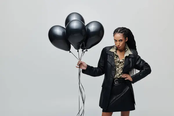 Une jeune femme élégante dans une veste et une jupe en cuir noir pose avec un tas de ballons noirs. — Photo de stock